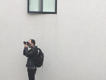Man photographing from camera while standing by wall