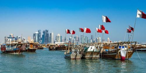 Sailboats moored at harbor against sky in city