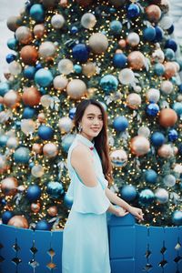Portrait of smiling young woman standing by christmas tree outdoors