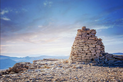 Stone stack on rock by building against sky