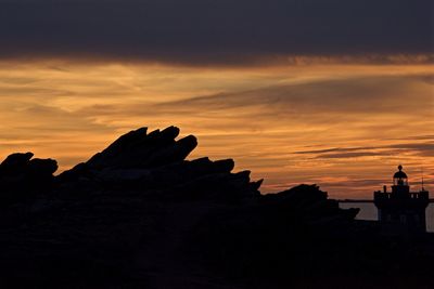 Silhouette cliff by sea against orange sky