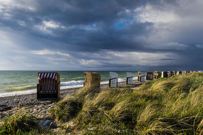 Hooded chairs at beach against cloudy sky