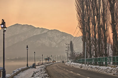 Road by snow covered mountains against sky during sunset