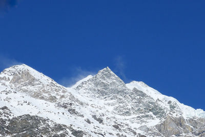 Low angle view of snowcapped mountains against clear blue sky