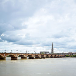 Arch bridge over river by church against cloudy sky in city