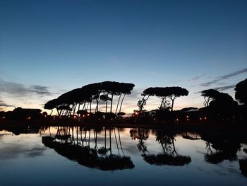 Silhouette trees by lake against sky during sunset