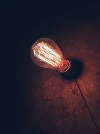 Low angle view of illuminated light bulb against wall