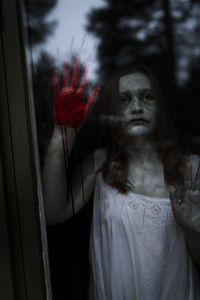 Female ghost with blood on hand seen through window of haunted cabin