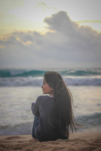 Girl sitting at beach against sky