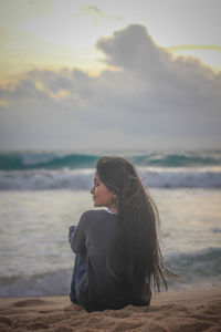 Young woman sitting on beach against sky