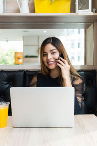Portrait of smiling businesswoman talking on phone while sitting by laptop