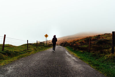 Rear view of person walking on road against clear sky