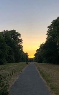 Road amidst trees against sky during sunset