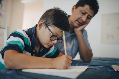 Father teaching disabled son while sitting at table