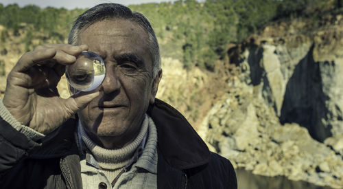 Close-up portrait of man holding sphere against rock formations