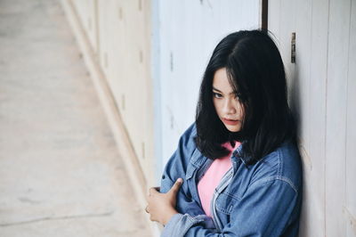 Thoughtful woman wearing denim jacket while looking away against wall