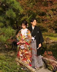 Young couple standing by plants against trees