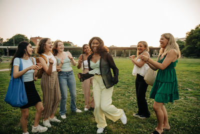 Teenage girls cheering friend dancing in park at sunset