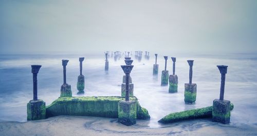 Old broken bridge in sea against sky during foggy weather