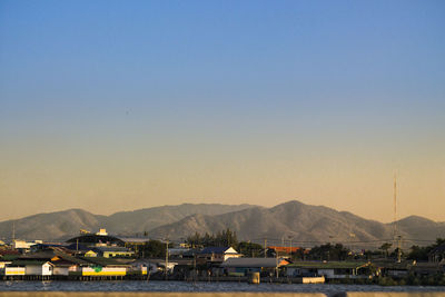 Sailboats in city by mountains against clear sky