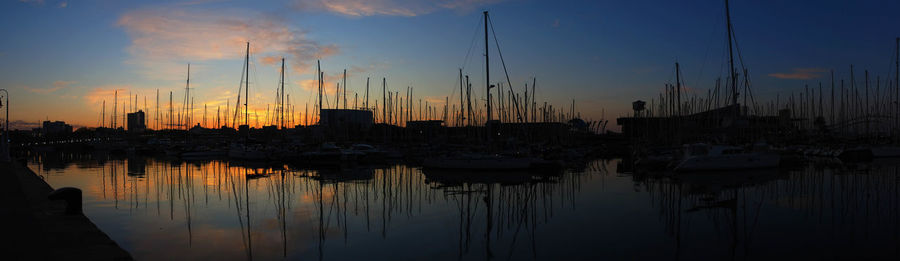 Sailboats moored at harbor against sky during sunset