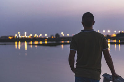 Rear view of man looking at illuminated city against sky