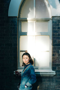 Portrait of a smiling young woman standing against window