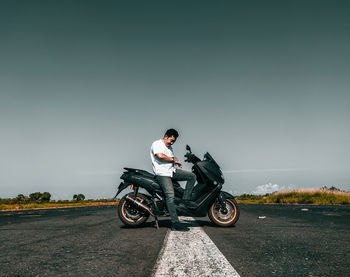 Side view of man riding motorcycle on road against sky