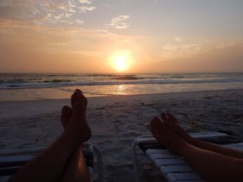 Low section of people at beach against sky during sunset