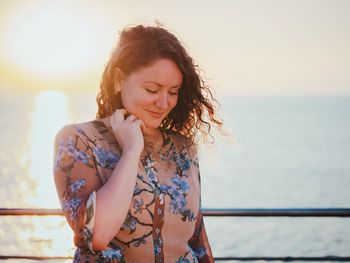 Beautiful young woman standing by sea against sky