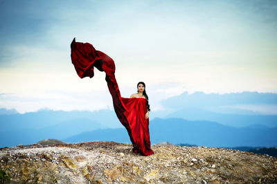 Portrait of young woman standing on mountain against sky