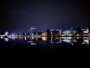 Illuminated buildings by river against sky at night