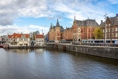 View of buildings by river against cloudy sky