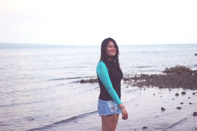 Young woman standing on beach against sky