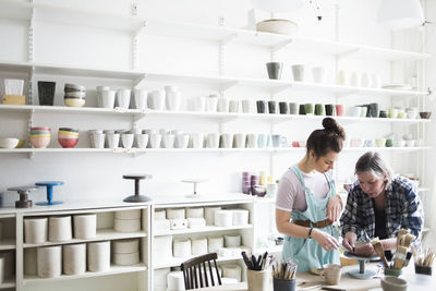 Mature female potter teaching molding clay to young artist at workshop