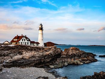 Lighthouse amidst buildings and sea against sky