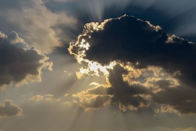 Low angle view of sunlight streaming through clouds