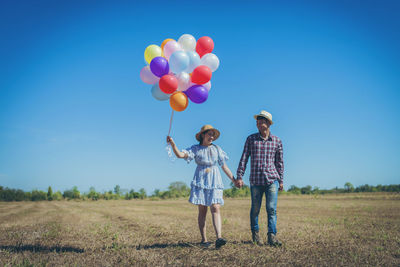 Rear view of man with balloons standing on field against blue sky