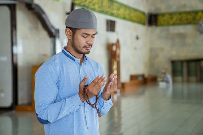 Young man wearing skull cap praying at mosque