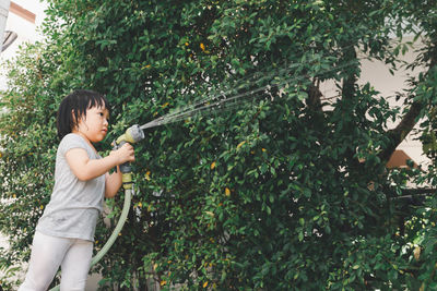 Funny moment of 3 year old asian kid playing water with garden hose in backyard. 