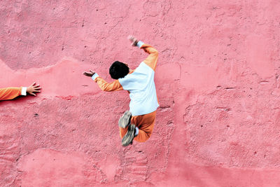 Full length of boy jumping in mid-air against pink wall