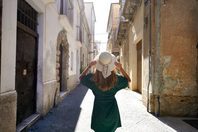 Back view of beautiful stylish tourist girl walking between narrow alleys of pizzo calabro, italy