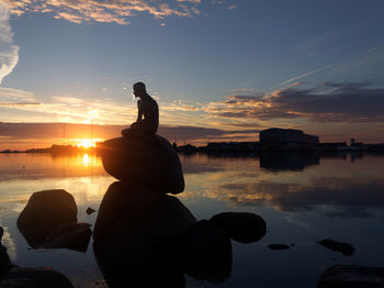 Silhouette of man sitting on rock at beach during sunset