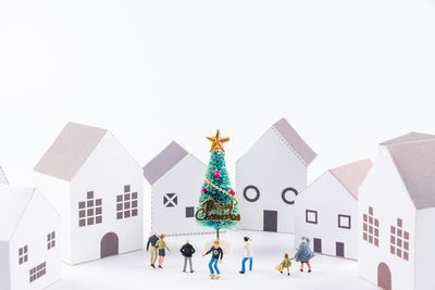 Close-up of figurines with christmas tree and model homes against white background