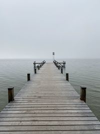 Wooden pier on jetty leading towards sea against clear sky