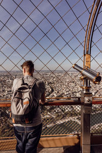 Rear view of man looking at railing against sky