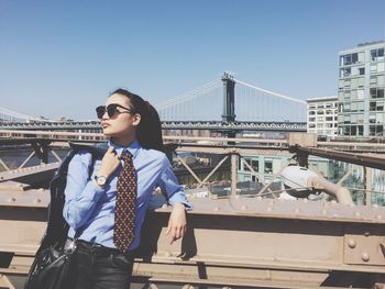 Businesswoman standing on brooklyn bridge against sky in city