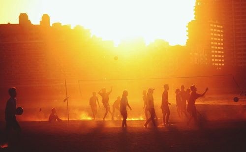 People playing beach volleyball at sunset