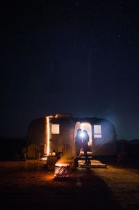 Man sitting in illuminated building against sky at night