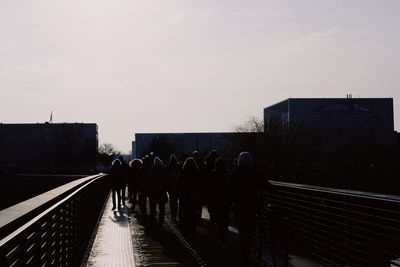 Rear view of people walking on road in city against sky